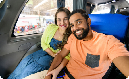 Imagem de um casal sorrindo para um selfie dentro do ônibus da Águia Abranca antes de começar uma viagem